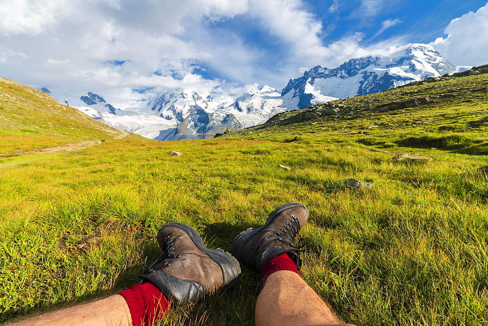 Hiker rests on grass looking towards Monte Rosa massif, Riffelalp, Zermatt, canton of Valais, Swiss Alps, Switzerland, Europe