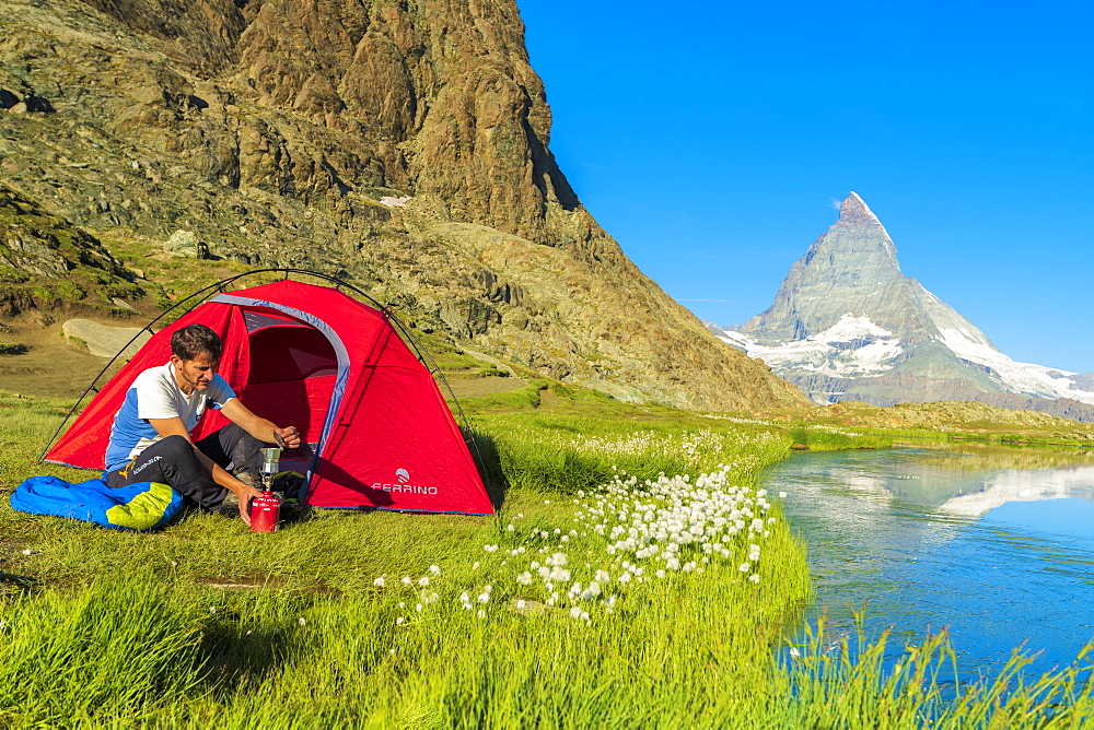 Hiker at lake Riffelsee makes coffee outside tent facing the Matterhorn, Zermatt, canton of Valais, Swiss Alps, Switzerland, Europe