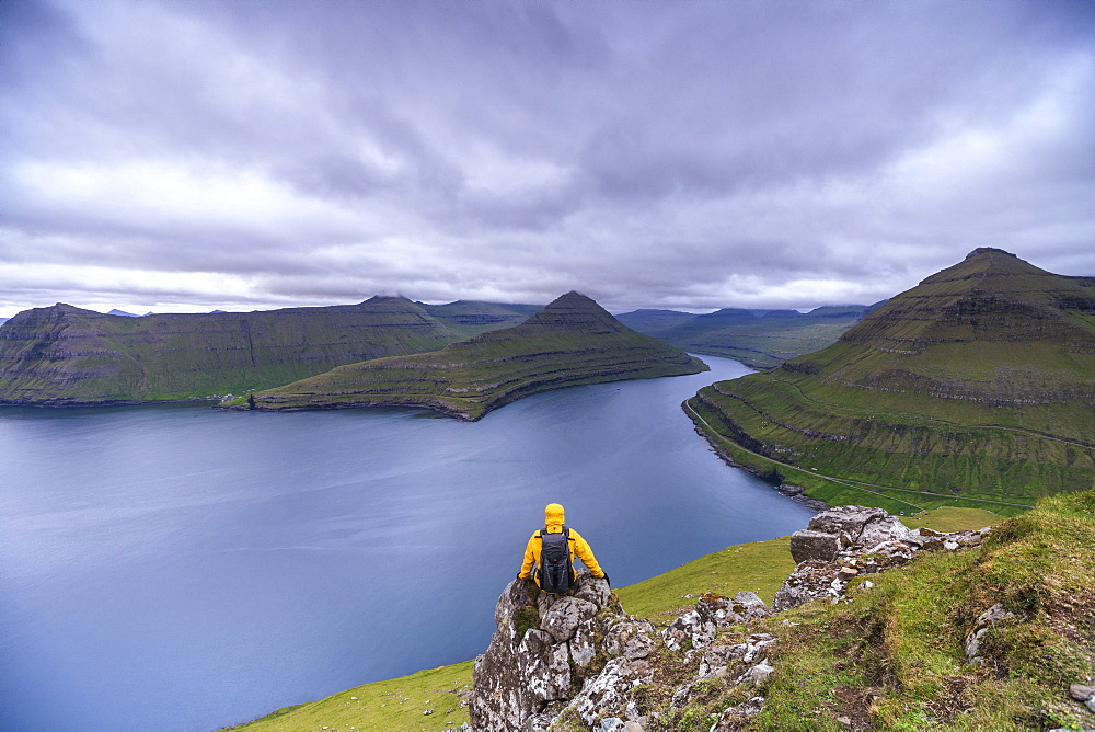 Hiker sitting on rocks looking at the fjords, Funningur, Eysturoy island, Faroe Islands, Denmark, Europe