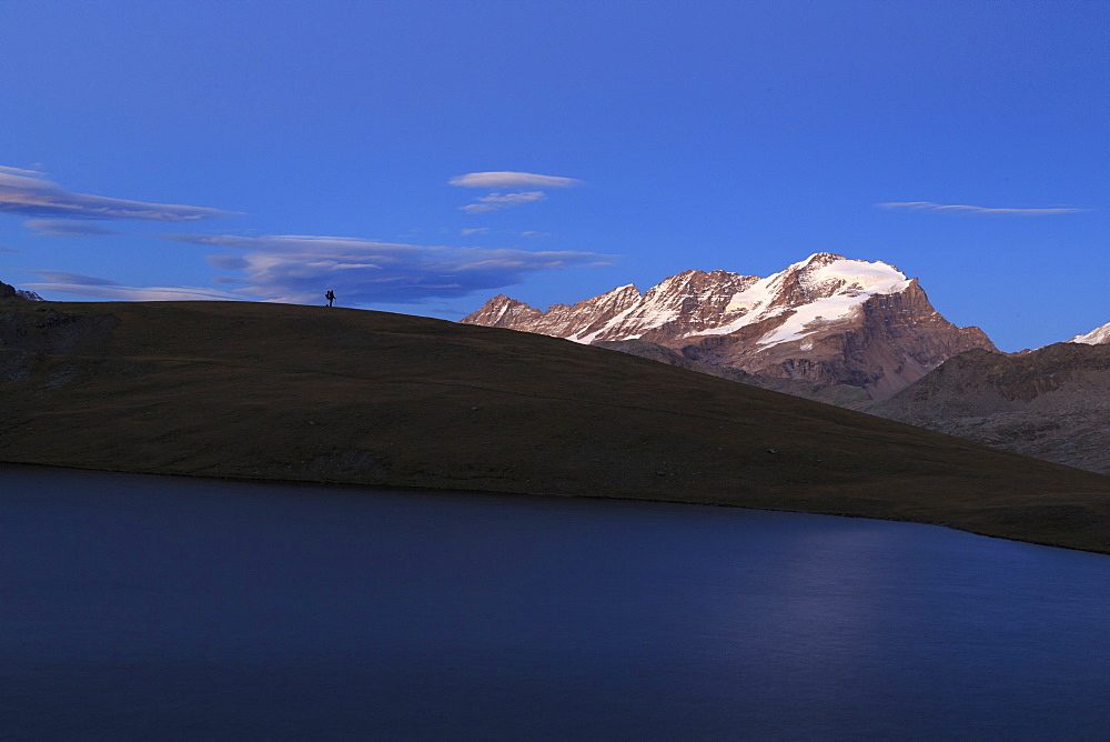 Hiker admires sunset on Rossett Lake at an altitude of 2709 meters, Gran Paradiso National Park, Alpi Graie (Graian Alps), Italy, Europe 