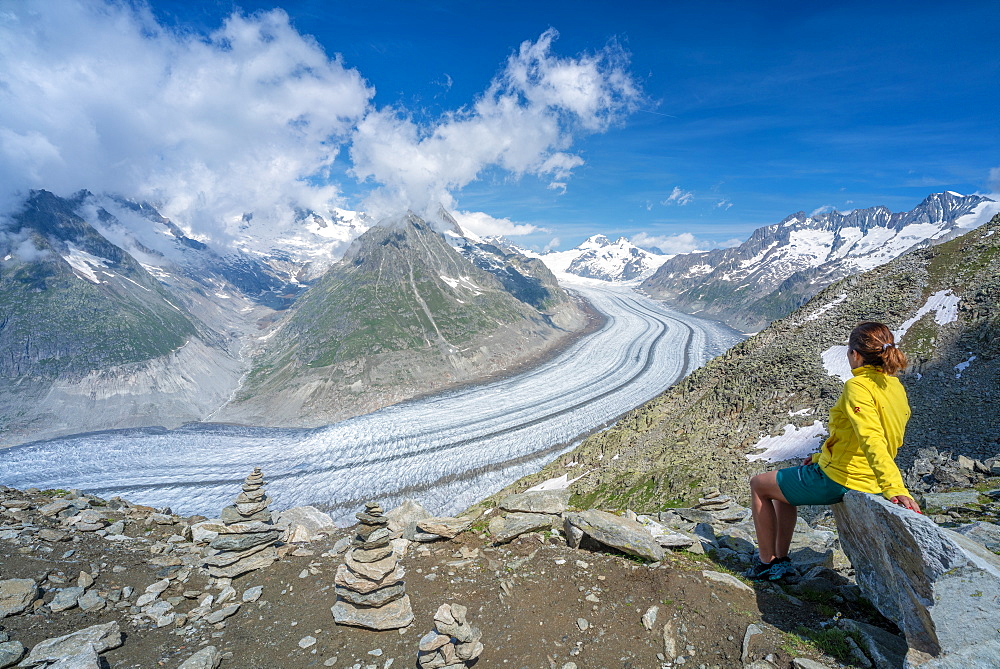 Side view of woman sitting on rocks admiring Aletsch Glacier from Eggishorn viewpoint, Bernese Alps, canton Valais, Switzerland, Europe