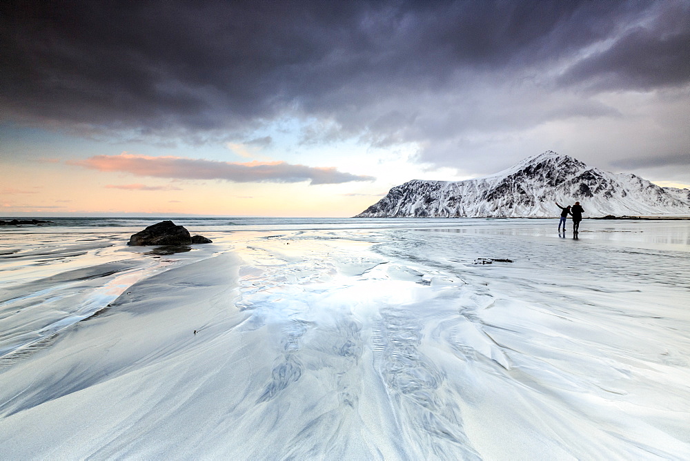 Sunset and hikers on Skagsanden beach surrounded by snow covered mountains, Flakstad, Lofoten Islands, Arctic, Norway, Scandinavia, Europe