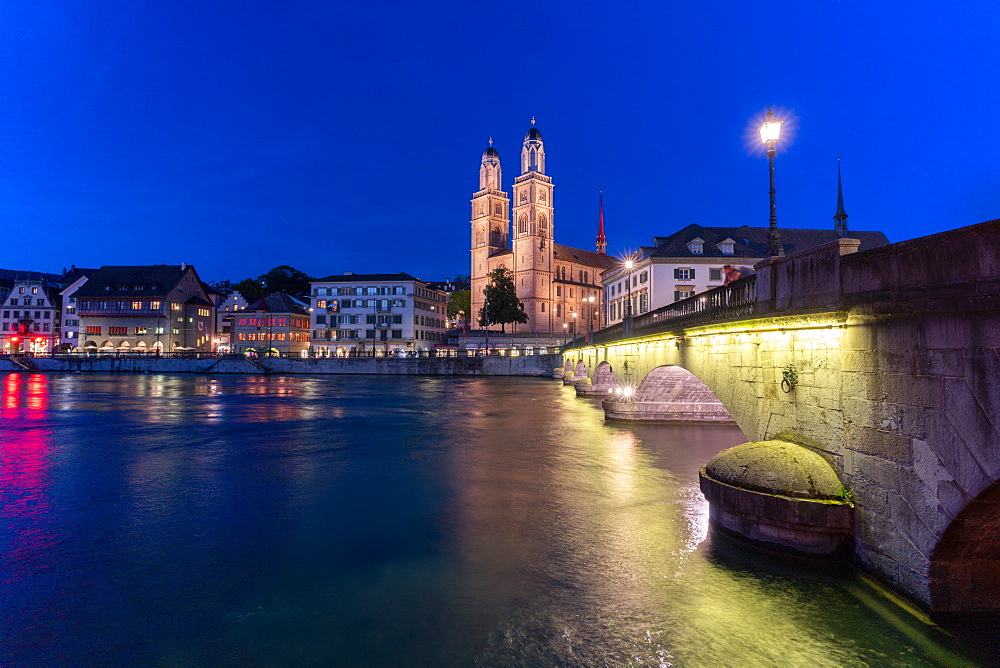 Illuminated buildings of Limmatquai and Grossmunster at dusk from Munsterbrucke bridge, Zurich, Switzerland, Europe