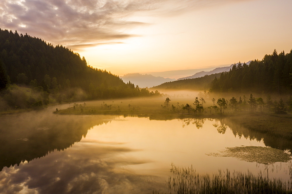 Sky painted orange at dawn with misty land of Pian di Gembro nature Reserve, aerial view, Aprica, Valtellina, Lombardy, Italy, Europe