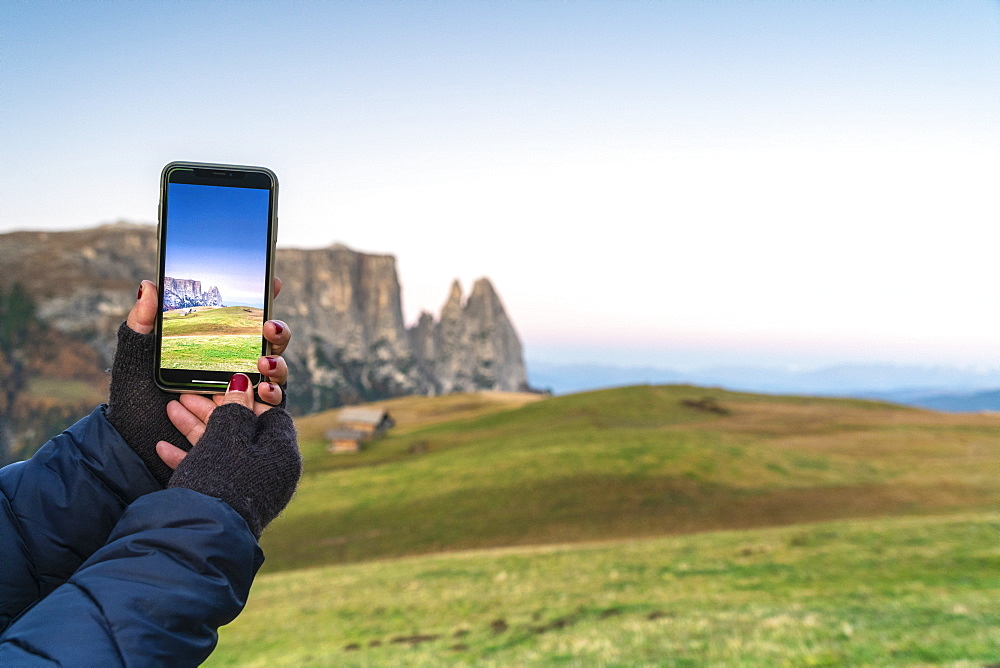 Personal perspective of woman photographing Sciliar peaks with smartphone, Alpe Siusi (Seiser Alm), Dolomites, South Tyrol, Italy, Europe