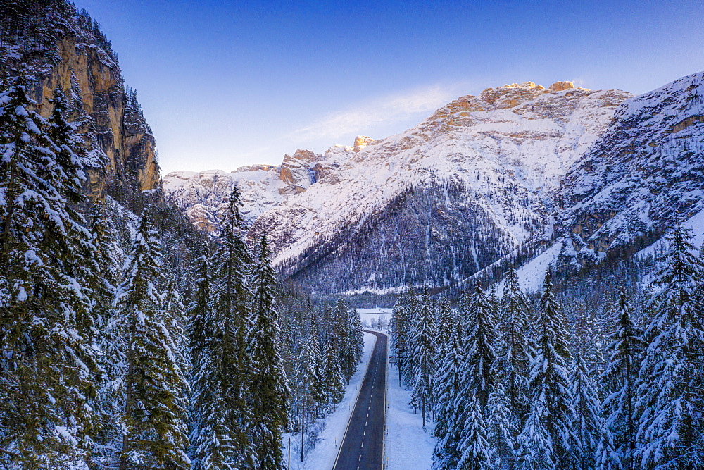 Aerial view by drone of sunrise on the scenic road Dobbiaco-Misurina along snowy woods, Dolomites, South Tyrol, Italy, Europe