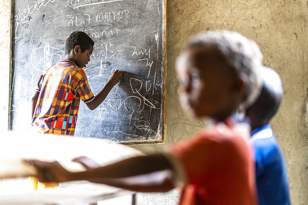 Young boy writing on blackboard at school, Melabday, Asso Bhole, Danakil Depression, Afar Region, Ethiopia, Africa