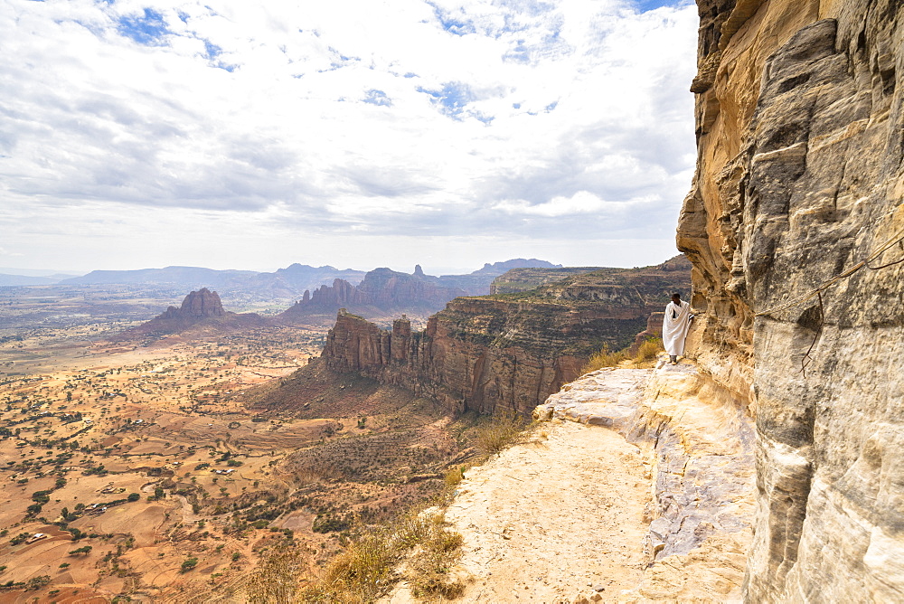 Orthodox priest standing on steep rocks at the entrance of Daniel Korkor church, Gheralta Mountains, Tigray Region, Ethiopia, Africa