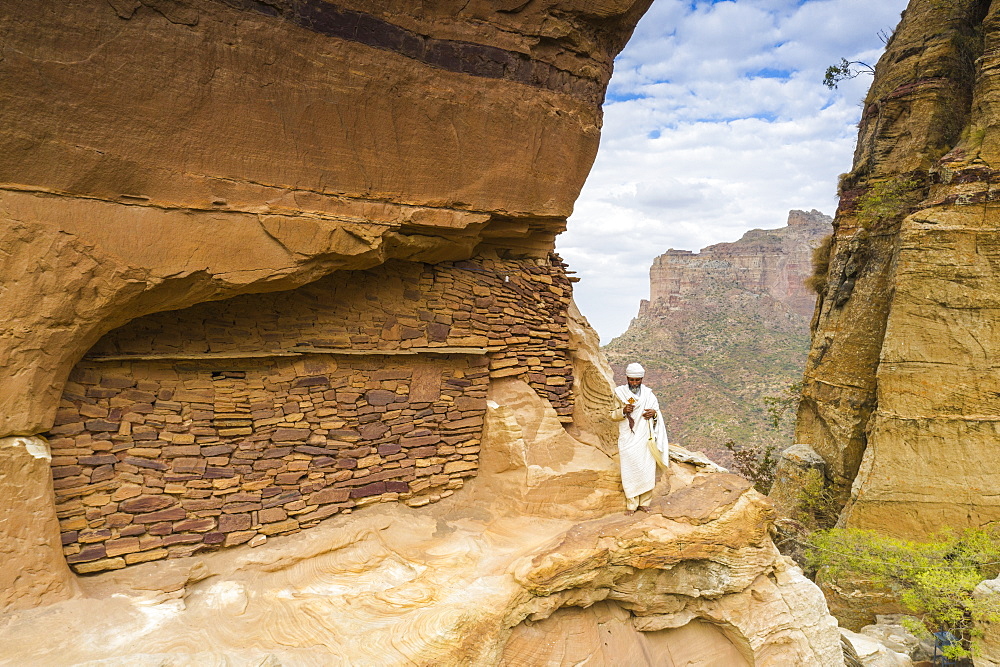 Priest holding the hand cross on rocks outside Abuna Yemata Guh church, Gheralta Mountains, Tigray Region, Ethiopia, Africa