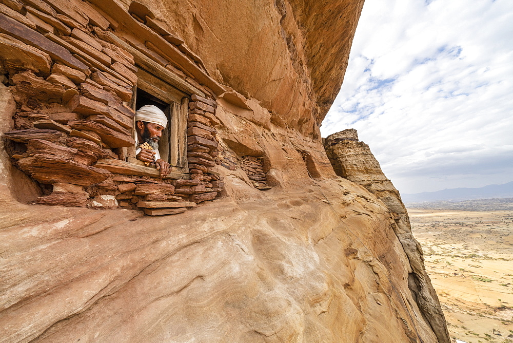 Priest looking out from a small window carved into rocks in Abuna Yemata Guh church, Gheralta Mountains, Tigray Region, Ethiopia, Africa