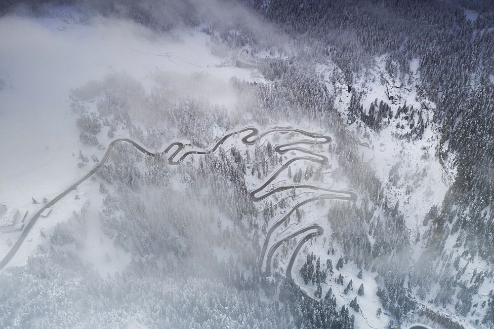 Fog on bends of Maloja Pass road and snowy woods, aerial view, Bregaglia Valley, Engadine, canton of Graubunden, Switzerland, Europe