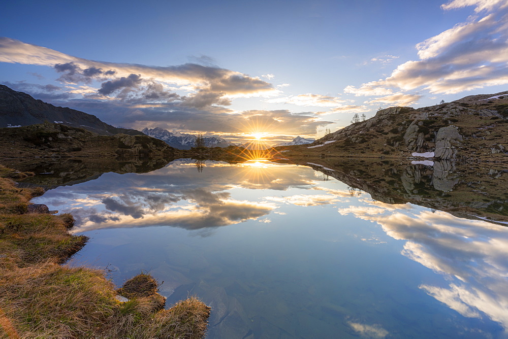 Sunburst over the clear waters of lake Zana during sunrise, Valmalenco, Sondrio province, Valtellina, Lombardy, Italy, Europe