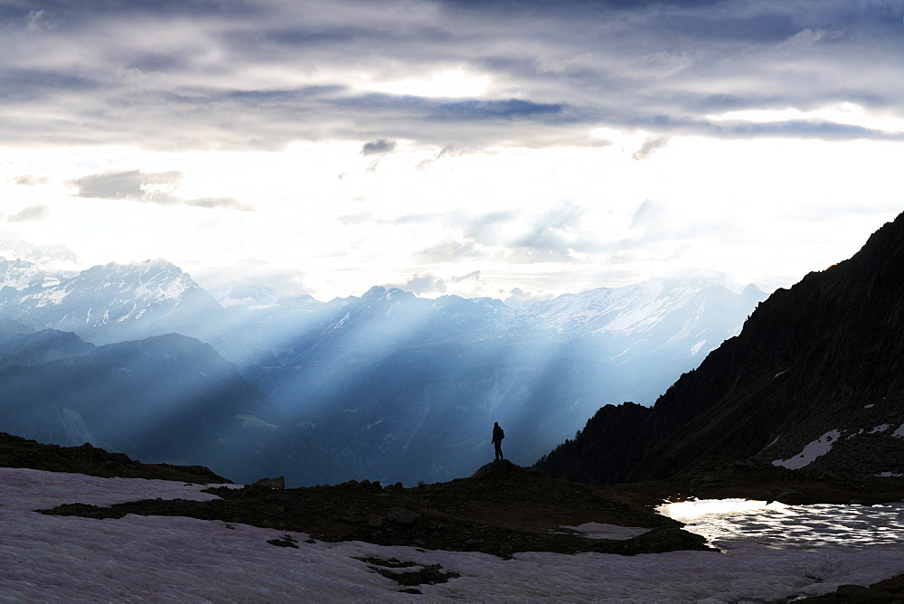 Silhouette of lone hiker admiring the sun rays at dawn over lake Zana, Valmalenco, Valtellina, Lombardy, Italy, Europe