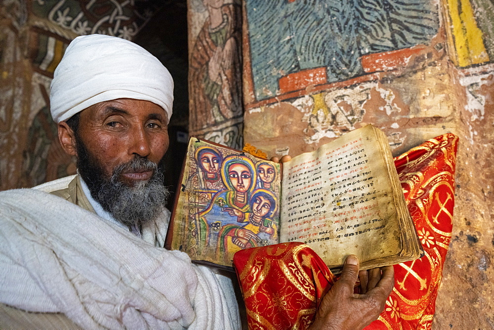 Orthodox priest holding an old Bible with hand-painted saints, Abuna Yemata Guh church, Gheralta Mountains,Tigray Region, Ethiopia, Africa