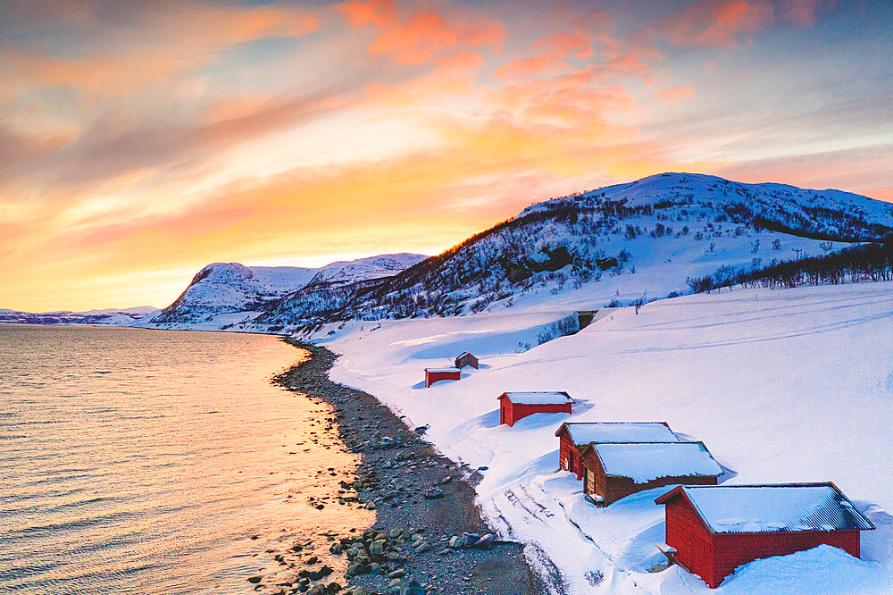 Sunset over red cabins in the snow along Porsangerfjord with North Cape (Nordkapp) on background, Troms og Finnmark, Arctic, Norway, Scandinavia, Europe