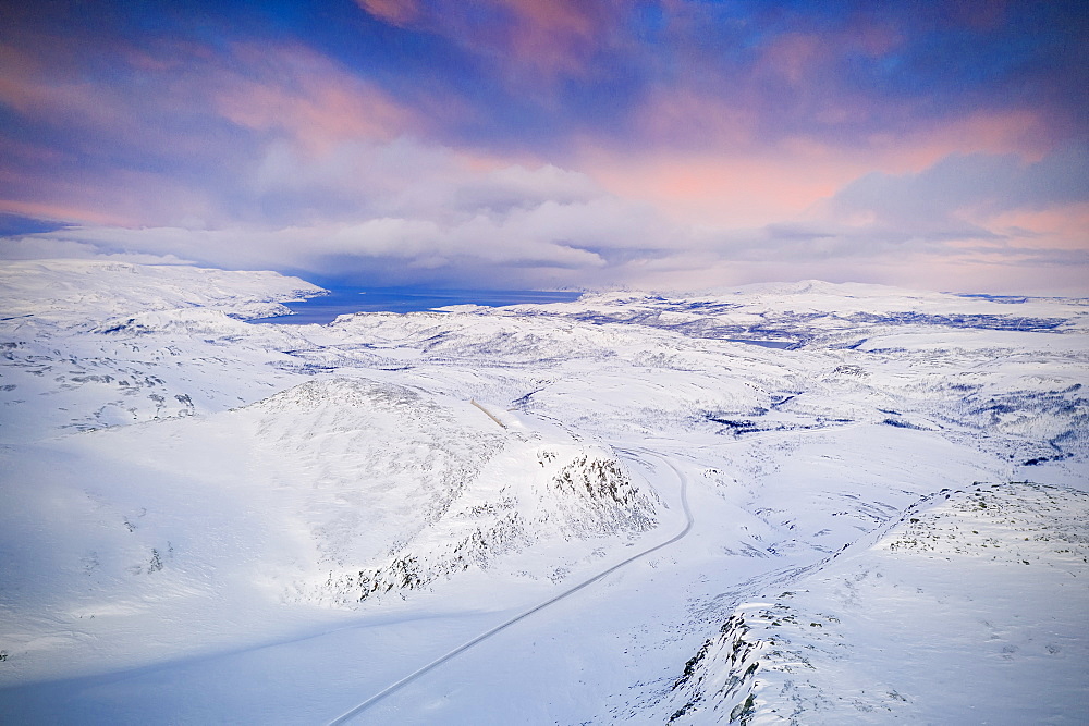 Pink sky at sunrise over Tanafjordveien road crossing the snow capped mountains, Tana, Troms og Finnmark, Arctic, Northern Norway, Scandinavia, Europe