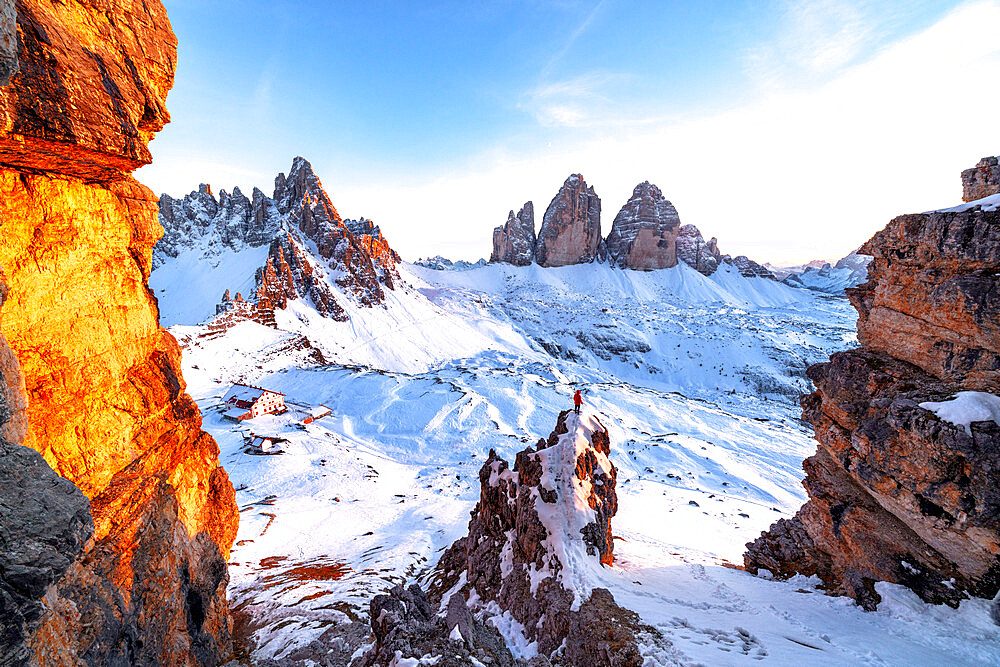 Man on rocks admiring the snowy Monte Paterno and Tre Cime di Lavaredo at sunset, Sesto Dolomites, South Tyrol, Italy, Europe