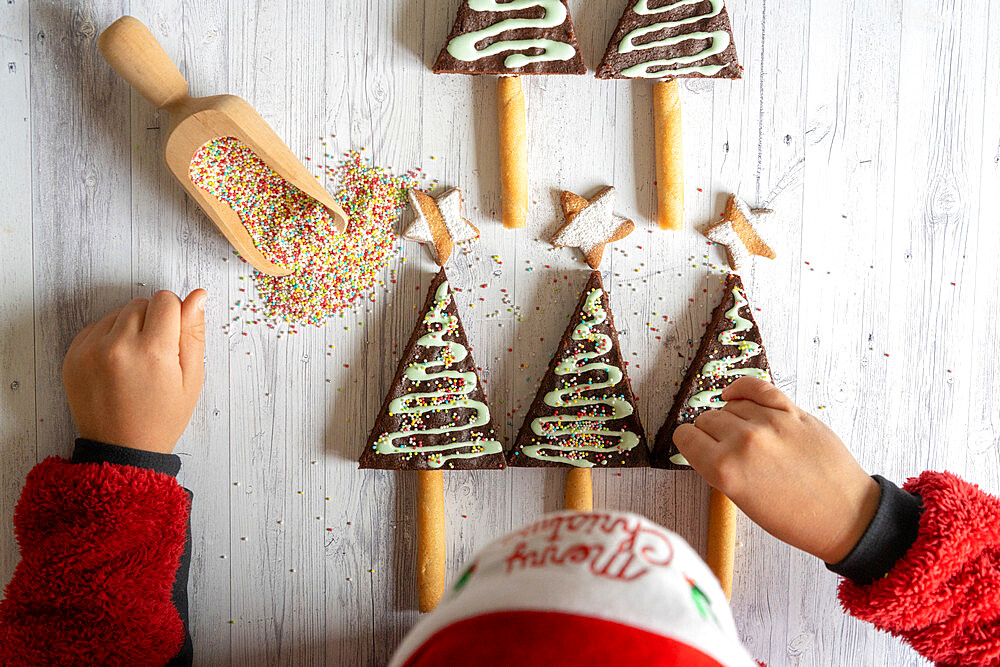 Overhead view of little child with Santa hat decorating the home made chocolate brownies and cookies in shape of Christmas tree, Italy, Europe