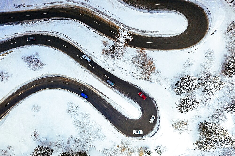 Aerial view of cars driving on bends of snowy mountain road in winter, Switzerland, Europe