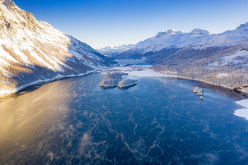 Snowcapped mountains frame the village of Sils Maria and frozen Lake Sils at sunrise, aerial view, Engadine, Graubunden Canton, Switzerland, Europe