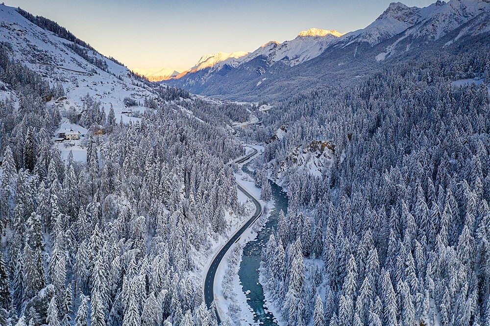 Sunrise over winding mountain road and frozen river in the forest covered with snow, Zernez, Graubunden Canton, Switzerland, Europe