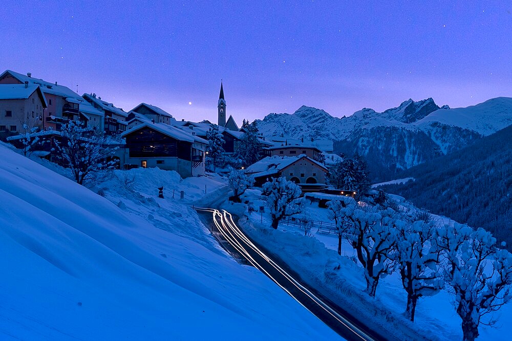 Snow covered village of Guarda lit by car trail lights during a blue winter dusk, Lower Engadine, Graubunden Canton, Switzerland,  Europe