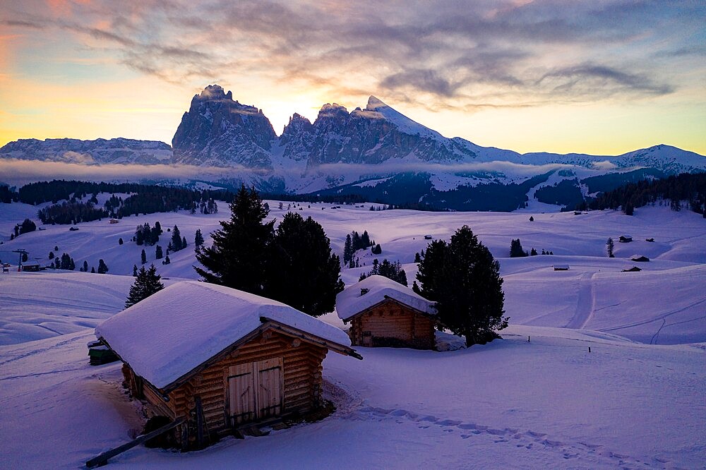 Wood cabins covered with snow with Sassopiatto and Sassolungo in background at dawn, Seiser Alm, Dolomites, South Tyrol, Italy, Europe