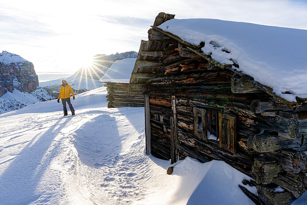 Hiker man in the snowy landscape lit by the backlight sunset in winter, Passo Gardena, Dolomites, South Tyrol, Italy, Europe