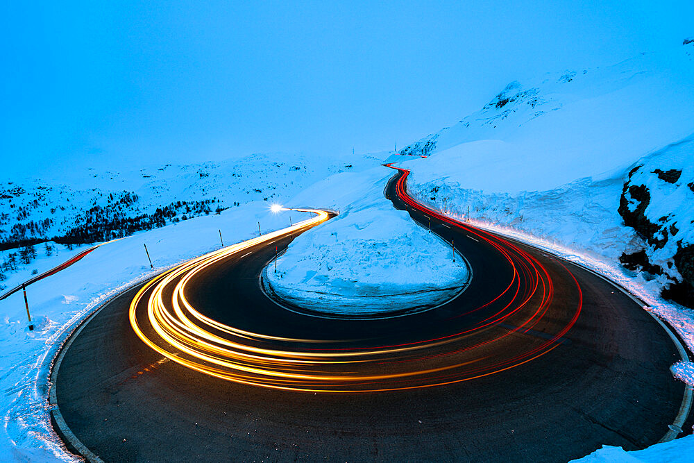 Car trail lights on bends of Bernina Pass road in winter, Val Poschiavo, canton of Graubunden, Engadin, Switzerland, Europe