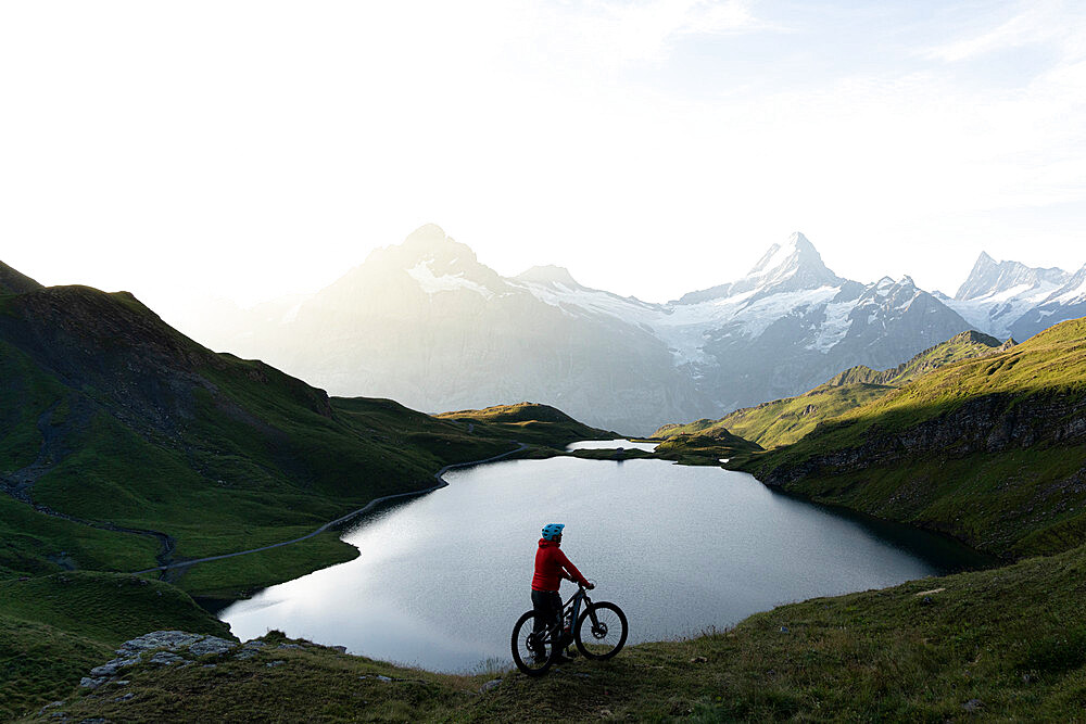 Hiker with mountain bike admiring sunrise over Bachalpsee lake, Grindelwald, Bernese Oberland, Bern Canton, Switzerland, Europe