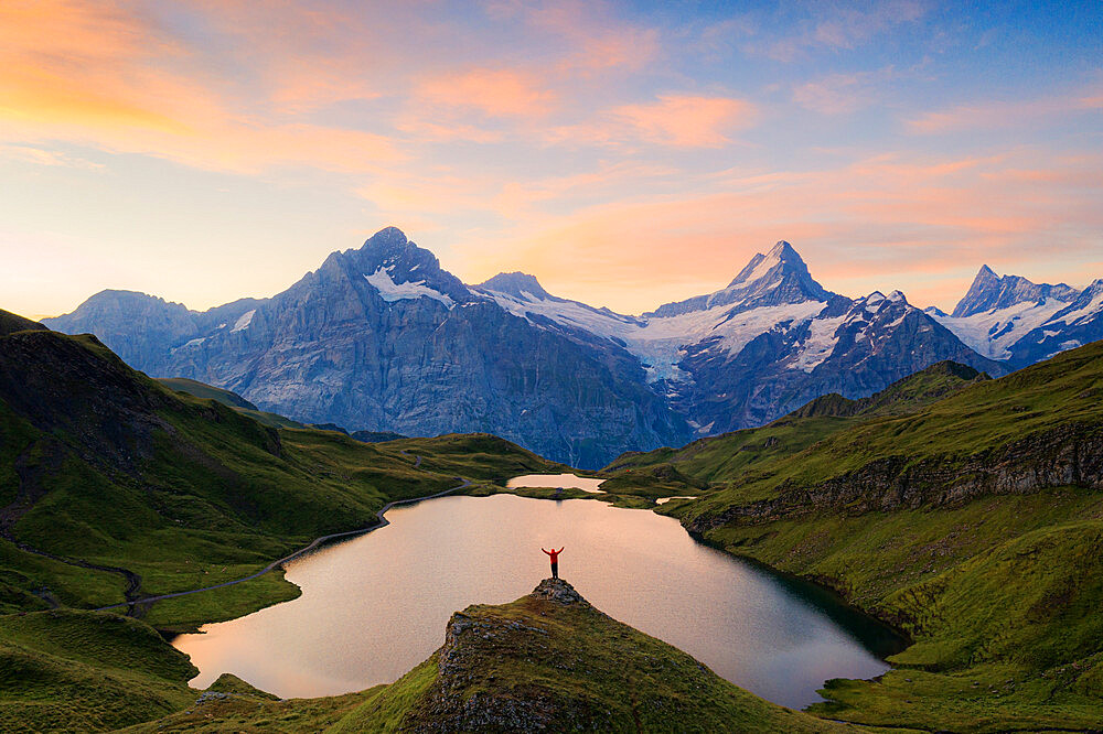 Cheerful hiker admiring Wetterhorn, Schreckhorn and Finsteraarhorn from Bachalpsee at dawn, Bernese Oberland, Switzerland, Europe