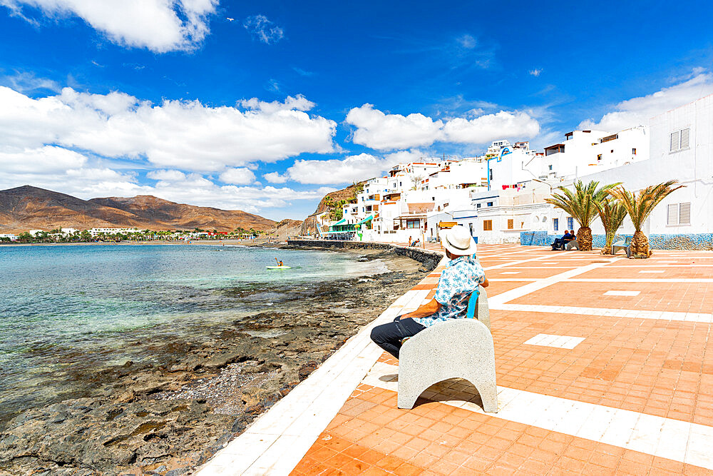 Tourist with straw hat admiring the ocean sitting on a bench in Las Playitas, Fuerteventura, Canary Islands, Spain, Atlantic, Europe