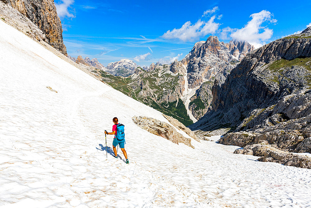 Hiker woman walking on snowy mountain ridge on path to Rifugio Locatelli hut, Sesto Dolomites, South Tyrol, Italy, Europe