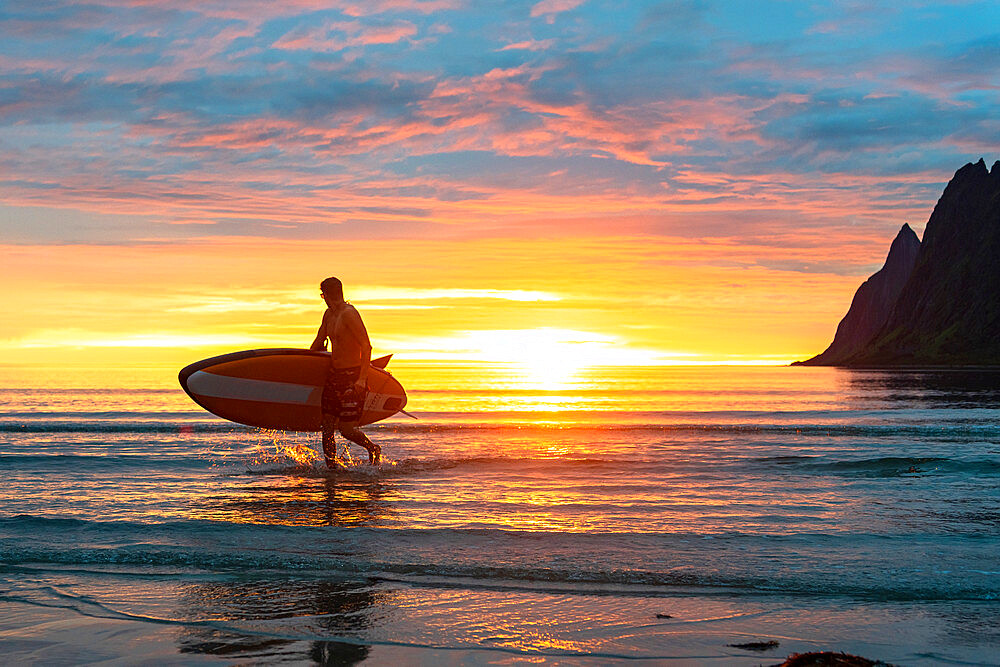 Stand up paddle boarder man admiring midnight sun walking back to the beach, Ersfjord, Senja, Troms county, Norway, Scandinavia, Europe