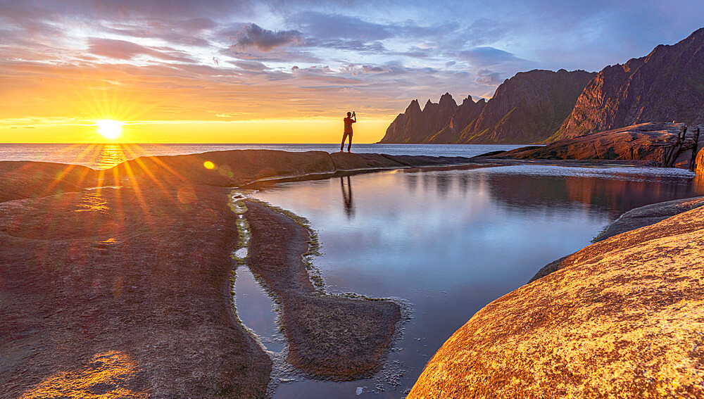 Man in the backlight sunset photographing the mountain peaks with smartphone, Tungeneset, Senja, Troms county, Norway, Scandinavia, Europe