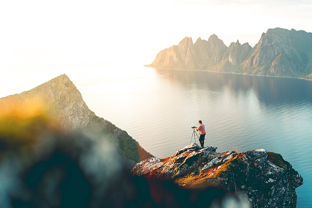 Photographer with tripod on Husfjellet mountain watching sunset on sharp peaks of mount Okshornan (Devil's Teeth), Senja, Norway, Scandinavia, Europe