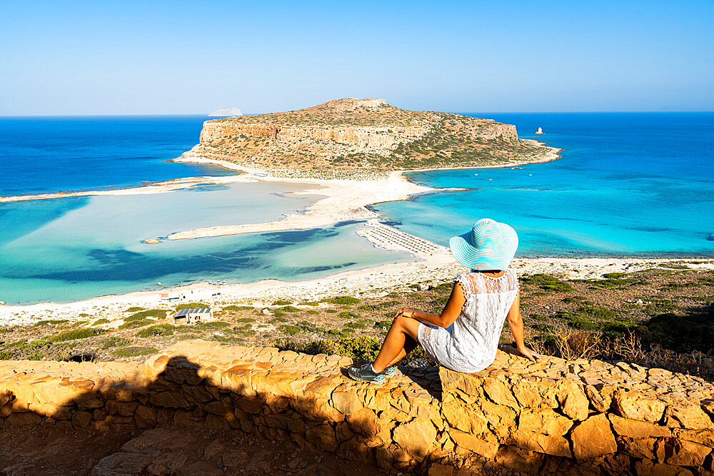 Charming woman with sundress and hat contemplating the crystal turquoise sea and lagoon, Balos, Crete, Greek Islands, Greece, Europe