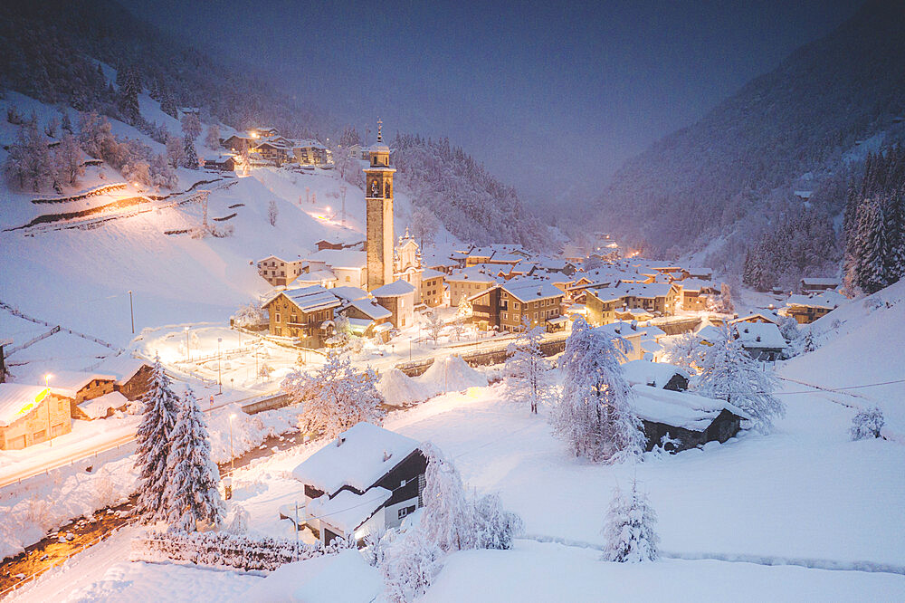 Illuminated village of Gerola Alta and frozen river covered with snow during winter dusk, Valgerola, Valtellina, Lombardy, Italy, Europe