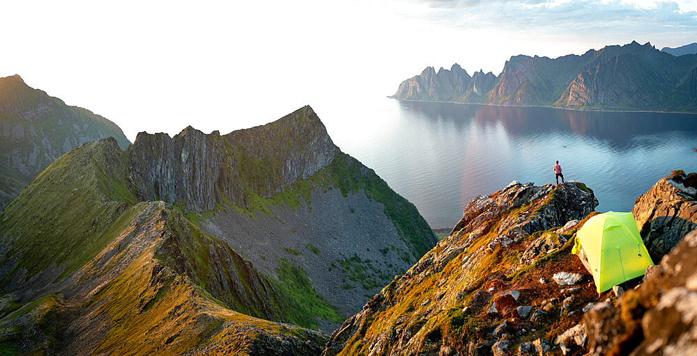 Tourist admiring sunset over the fjord out of camping tent, Senja island, Troms county, Norway, Scandinavia, Europe