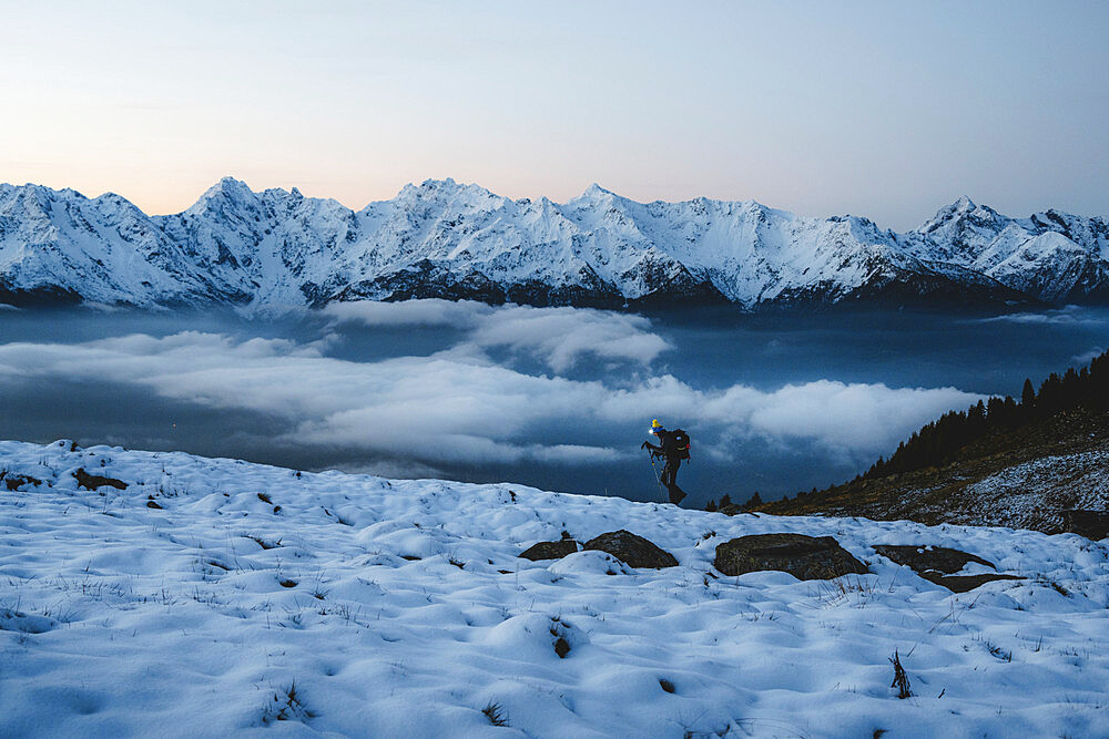 Man with hiking poles walking in the snow with majestic Orobie Alps in the background, Alpe Rogneda, Rhaetian Alps, Lombardy, Italy, Europe