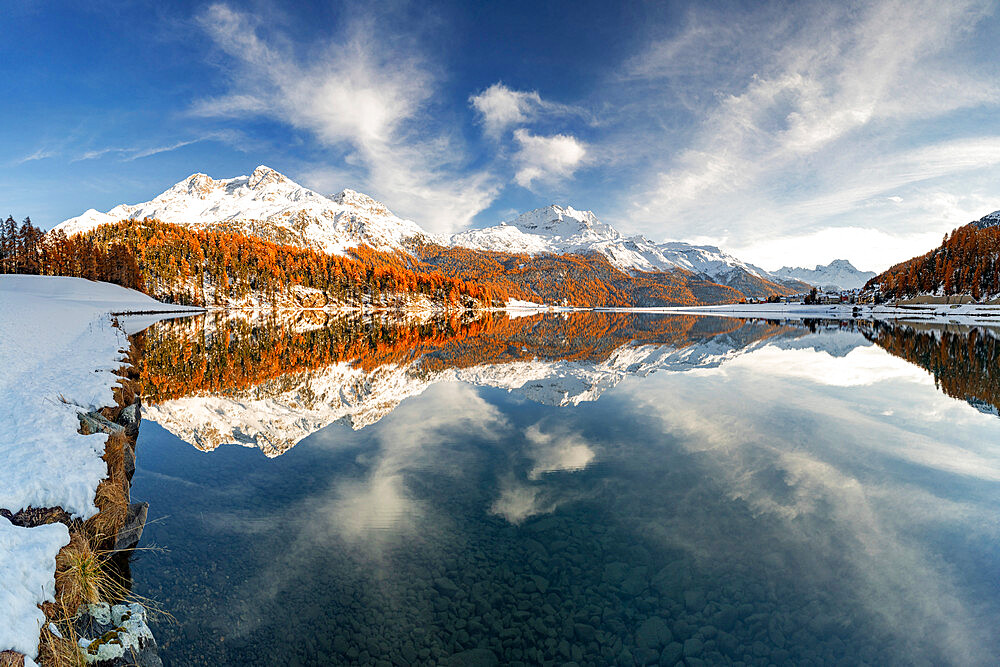 Autumn woods and snowcapped mountains mirrored in the clear water of Champfer lake at sunset, Engadine, Graubunden, Switzerland, Europe