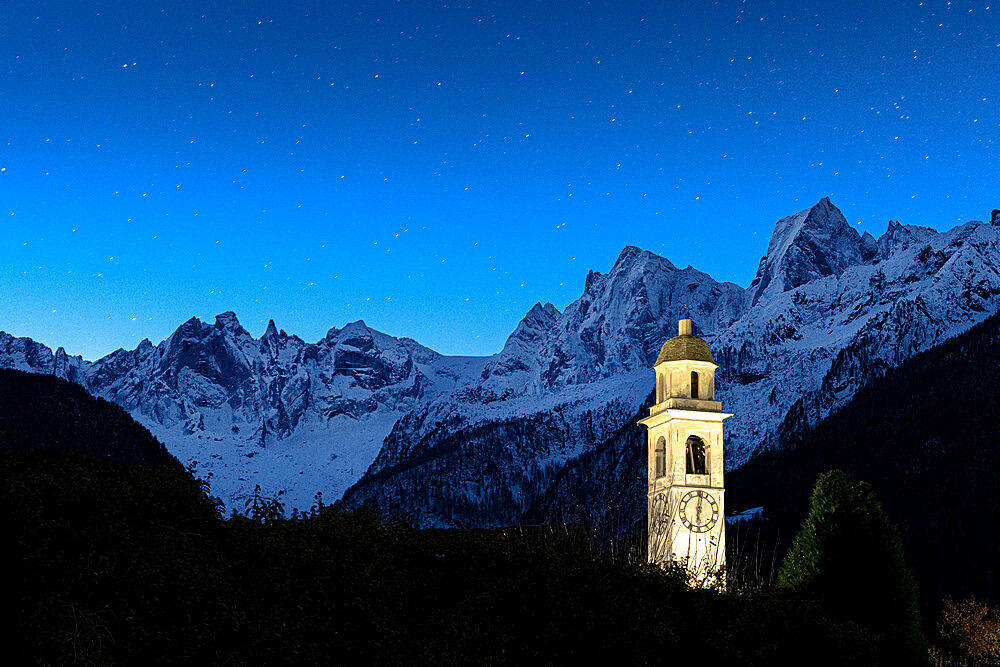 Illuminated bell tower and Sciore mountain range covered with snow under the starry sky, Soglio, Graubunden, Switzerland, Europe