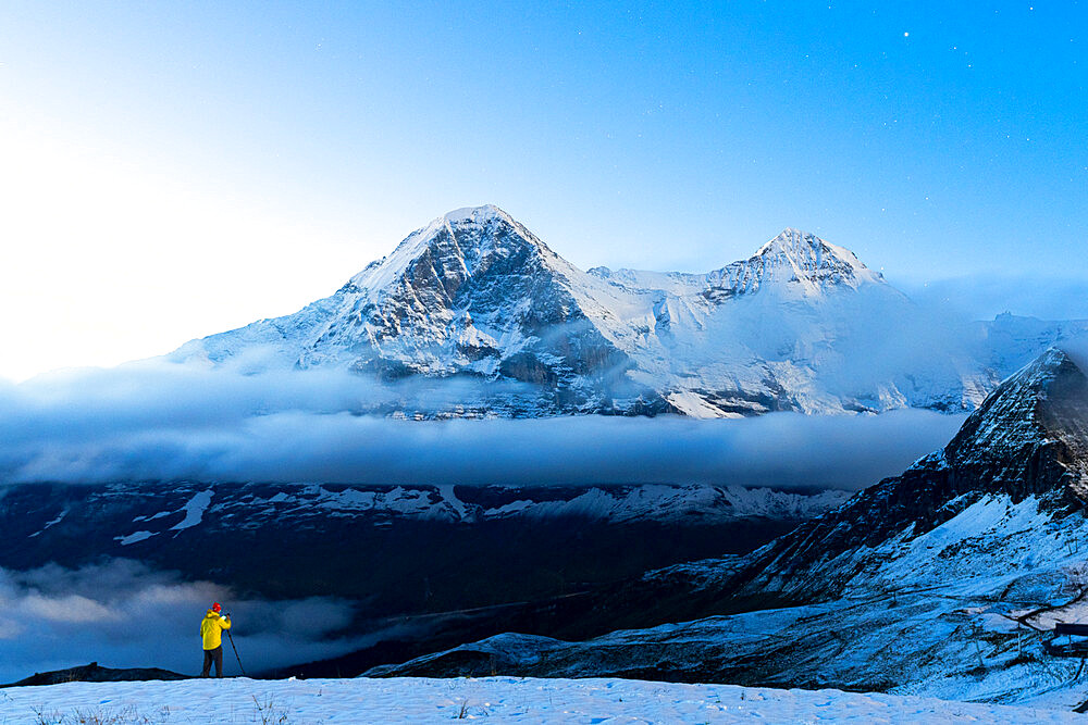 Man with tripod in the snow photographing Eiger and Monch mountain peaks at night, Mannlichen, Bern Canton, Swiss Alps, Switzerland, Europe