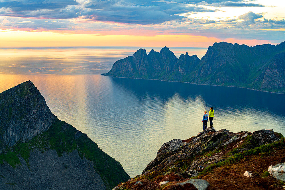 Two young women watching sunset standing on mountain top, Senja island, Troms county, Norway, Scandinavia, Europe