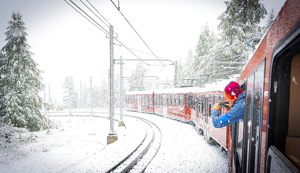 Man photographing the snow falling over mountains during a trip on board of Gornergrat Bahn train, Zermatt, Valais, Switzerland, Europe