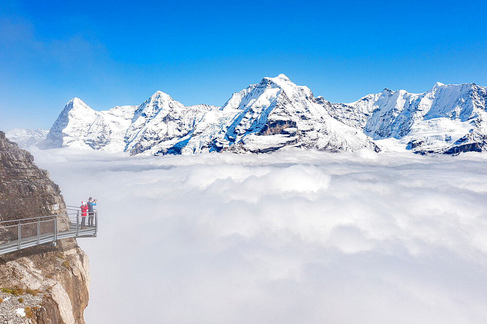 Two people photographing snowcapped Eiger and Monch peaks in fog from elevated walkway, Murren Birg, Bern canton, Swiss Alps, Switzerland, Europe