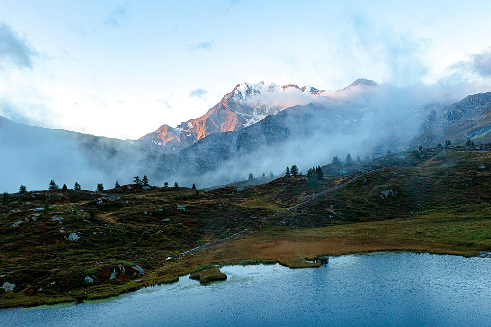 Aerial view of Fletschhorn and Galehorn mountains in fog at dawn from Hopschusee lake, Simplon Pass, Valais canton, Swiss Alps, Switzerland, Europe