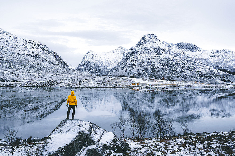 Person admiring the snowcapped mountains reflected in frozen sea, Flakstadpollen, Flakstadoya, Nordland, Lofoten Islands, Norway, Scandinavia, Europe