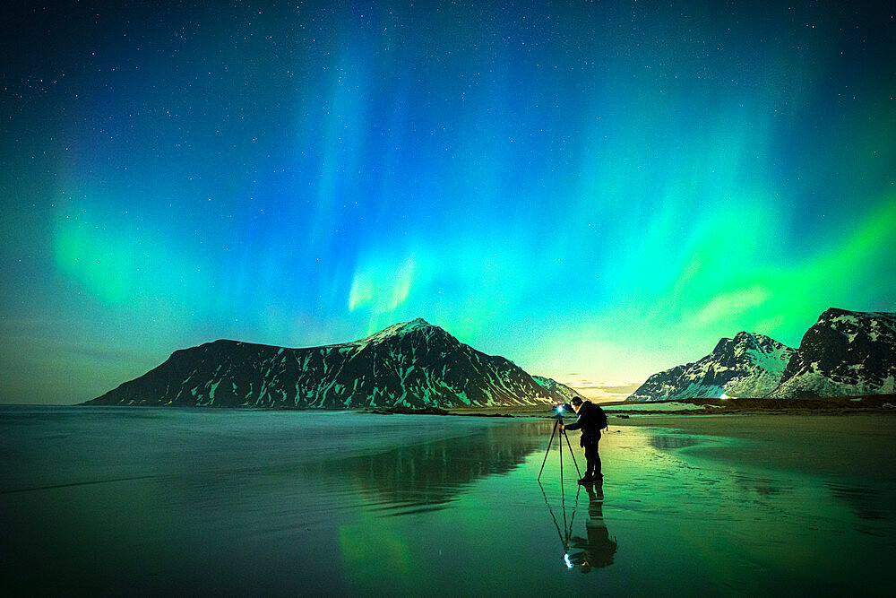 Person photographing the bright sky during Aurora Borealis (Northern Lights) standing on Skagsanden beach, Lofoten Islands, Norway, Scandinavia, Europe