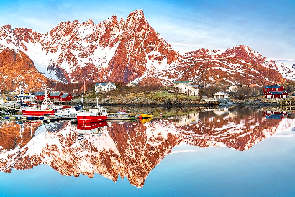 Fishing boats and snowcapped mountains mirrored in the fjord at sunrise, Ballstad, Vestvagoy, Lofoten Islands, Norway